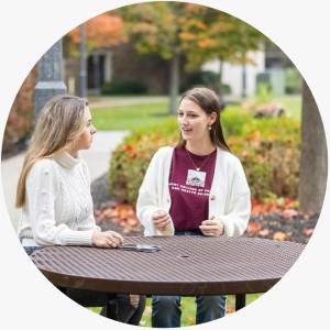 Two students have a discussion at a table outside on the ACPHS campus