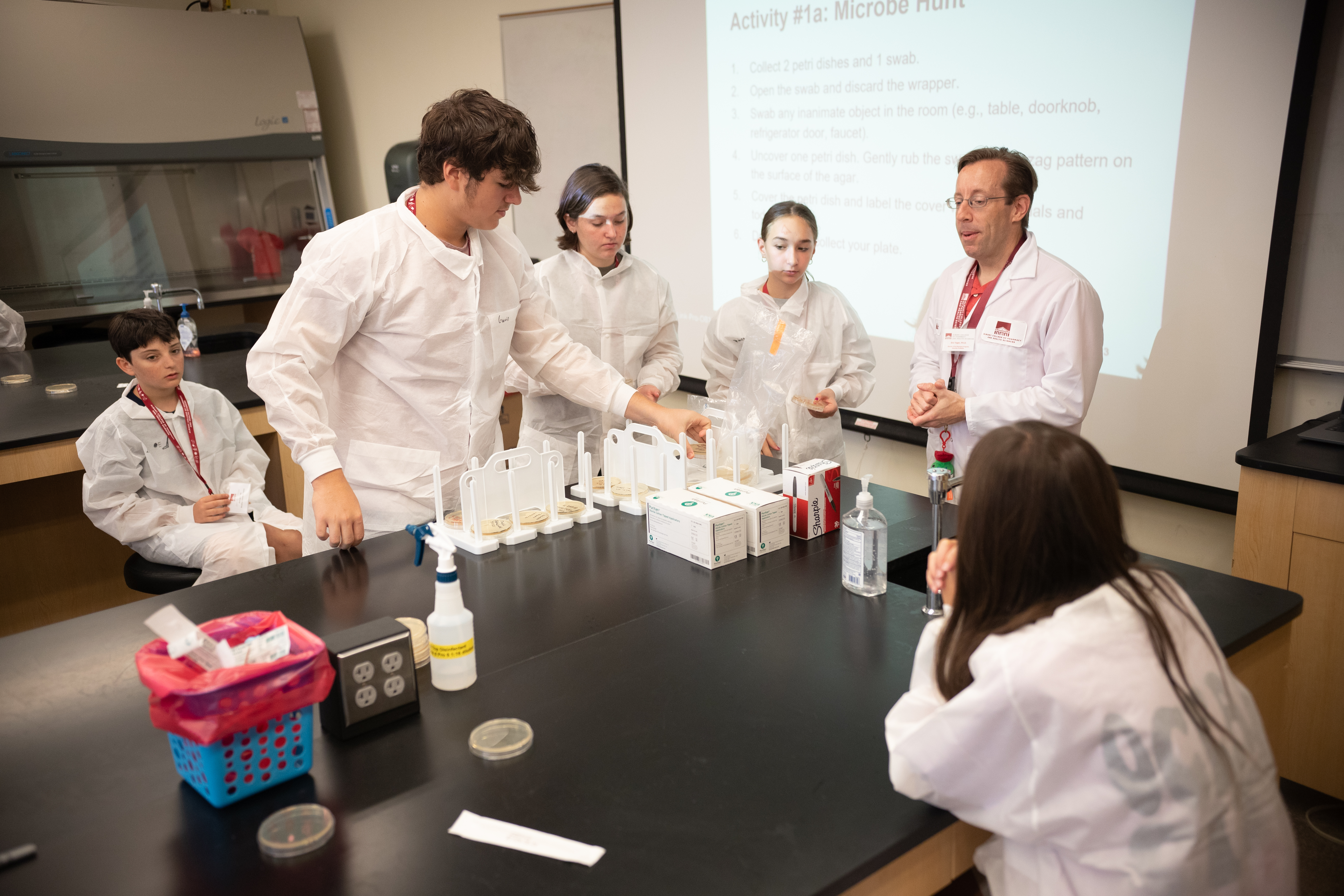 Students in white lab coats work in a lab during a summer camp.