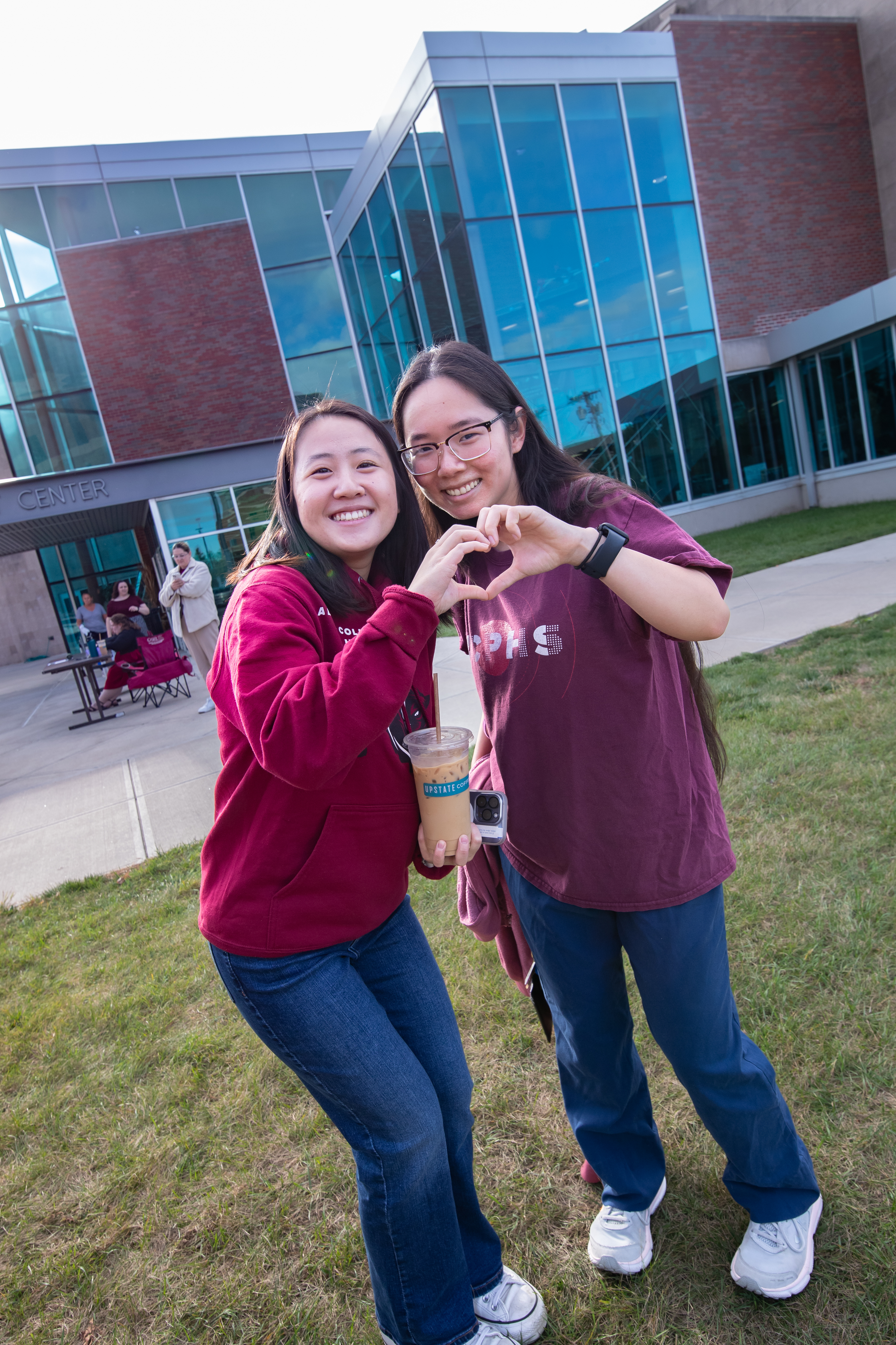 Two students stand together and put together hands to form heart shape