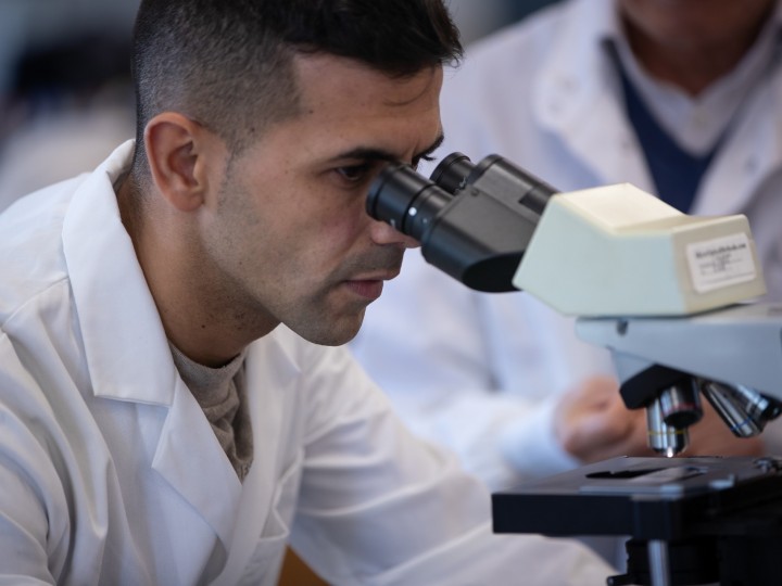 A student wears lab coat and looks into microscope